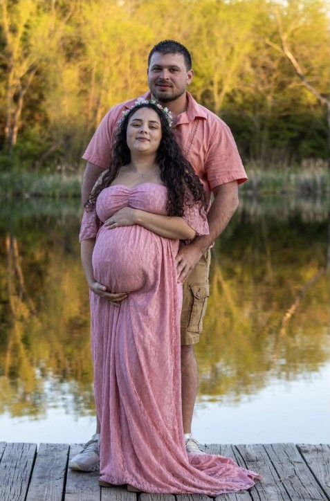 Maternity couple portrait beside reflective water at golden hour