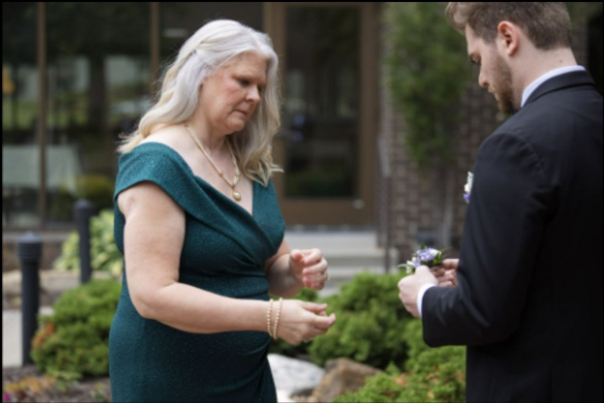 Woman helping groom with a boutonniere before the wedding